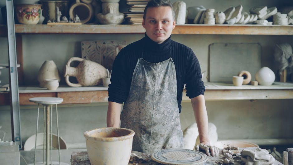 Craftsman in a potter's studio surrounded by handmade ceramics.